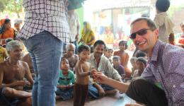 Mit Trommeln und Schellen wird das Team zum Versammlungsplatz geleitet, auf dem nach der Besprechung Süßigkeiten an die Kinder der Kolonie verteilt werden.