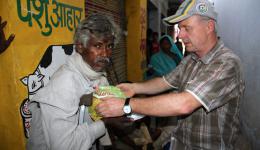 Hans drückt dem Leprabetroffenen einen 4 kg-Sack Dal in die behinderten Hände. Sein Sack Reis wird von einem Helfer in seine Hütte im Straßenslum gebracht.