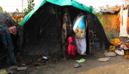 Die Leprakolonie in Samstipur, Bihar.  Hinter einem, mit Tüchern verhangenen Eingang, sitzt ein kleiner, älterer Mann. Einem seiner Beine fehlt der Unterschenkel. Der andere Fuß ist nur noch ein Stumpf. Ein Auge ist blind.