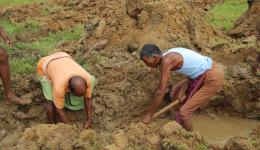 Die Erde wird mit Harken aufgelockert und aus dem Graben geworfen. Durch vereinzelte Regenschauer, den Vorboten des Monsun-Regens, entstehen bereits knietiefe Pfützen in den Gräben. Die Erde wird mit Harken aufgelockert und aus dem Graben geworfen. Durch vereinzelte Regenschauer, den Vorboten des Monsun-Regens, entstehen bereits knietiefe Pfützen in den Gräben.
