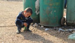 Ein Junge spielt mit einer Flasche und befüllt sie mit Kieselsteinen.