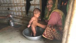 The mother bathes her baby in a bowl.